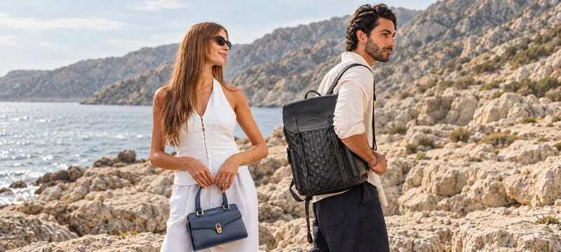 A woman with a navy Luffy handbag and a man with a black Luffy backpack by the coast